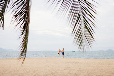 Rear view of couple running on beach against sky