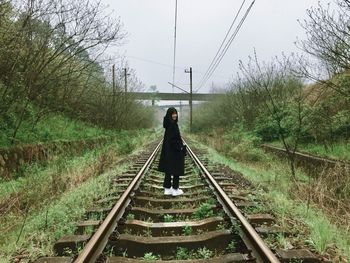 Rear view of woman on railroad amidst trees against sky