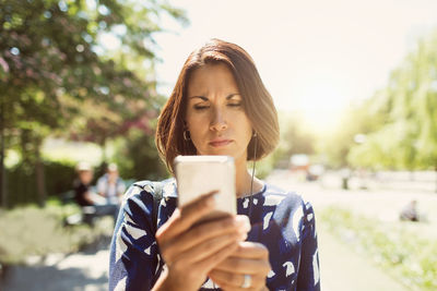 Mature businesswoman using smart phone in park during summer