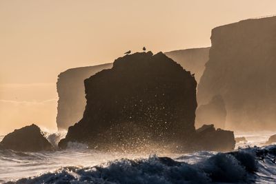 Rock formation in sea against clear sky during sunset