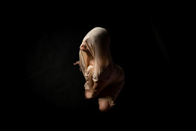 Woman covering face against black background