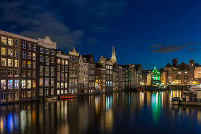 Illuminated buildings by river against sky at dusk