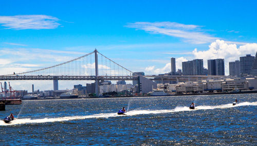 Tokyo rainbow bridge over sea against blue sky with jet skis in foreground