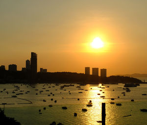 Silhouette buildings by sea against sky during sunset