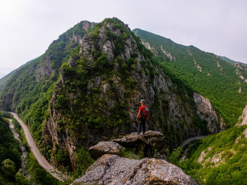 Man on rock by mountain against sky