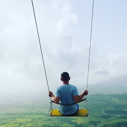 Rear view of man sitting on fishing rod against sky