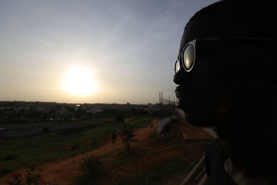 Portrait of man looking at camera on field against sky during sunset