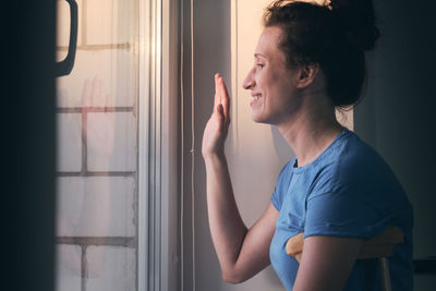 Woman on crutches stands at the window and waves her hand