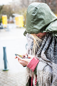 Woman in raincoat using mobile phone on street