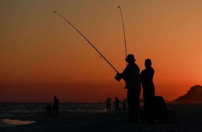 Silhouette people fishing at beach during sunset