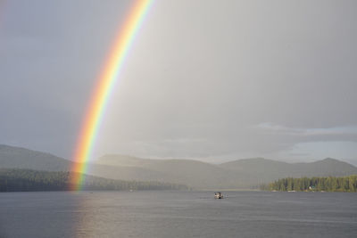 Vivid rainbow over calm lake with boat near shore in countryside