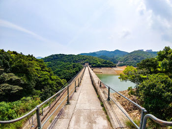 Footbridge amidst trees in forest against sky
