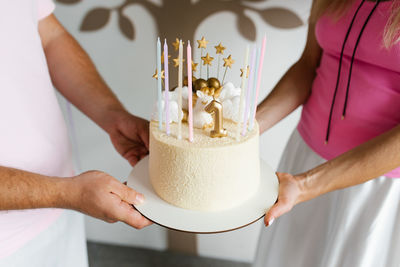 Hands of parents holding a beautifully decorated birthday cake with golden details and pastel