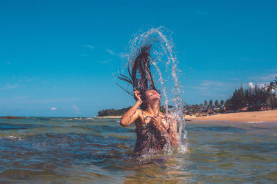 Woman splashing water in sea against sky