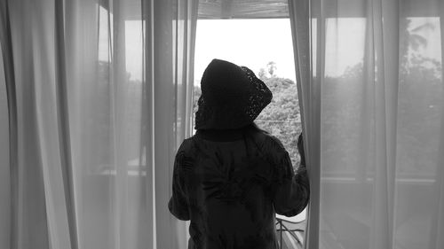 Rear view of woman looking through window at home