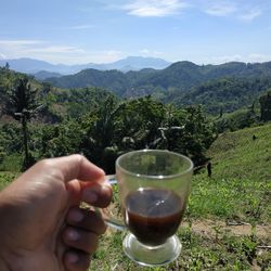 Cropped image of person holding drink by mountains