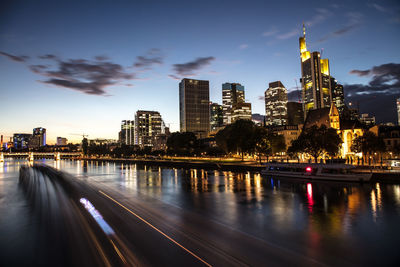 Illuminated buildings by river against sky in city at night