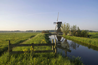 Traditional windmill on field by lake against clear sky