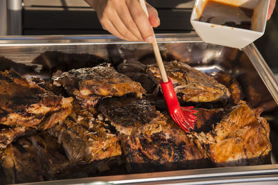 Cropped hand of person basting barbecue ribs