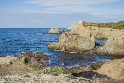 Rocks on shore by sea against sky