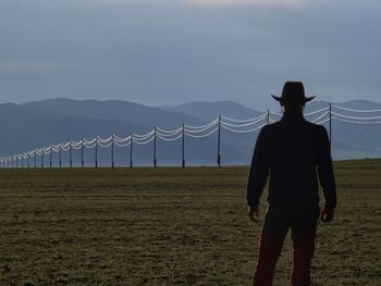 Rear view of man standing on field against sky