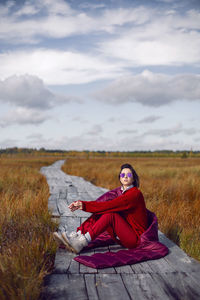 Woman  in red warm clothes and a big scarf on an ecological trail in the autumn not a swamp