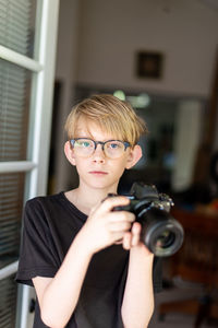 Tween making eye contact holding modern camera in doorway to home