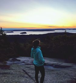 Rear view of woman standing on shore during sunset