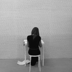 Rear view of woman sitting on chair against wall
