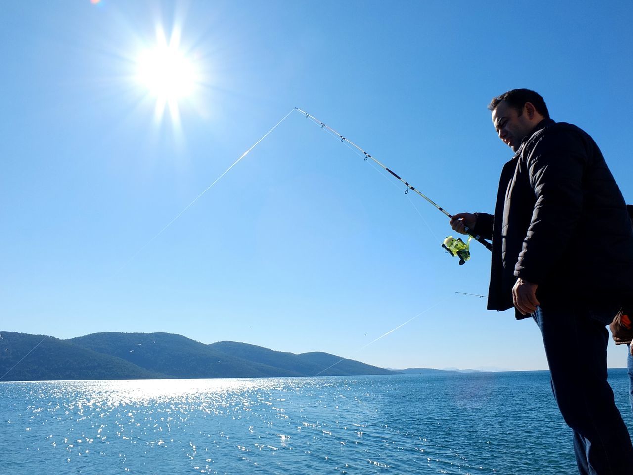 lifestyles, leisure activity, water, men, vacations, enjoyment, sea, clear sky, casual clothing, sunlight, blue, young adult, standing, full length, mountain, holding, sky