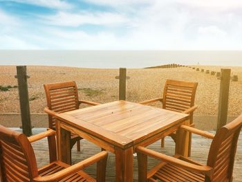Chairs and table on beach against sky