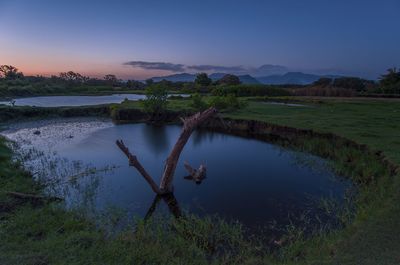 Pond by field against sky during sunset