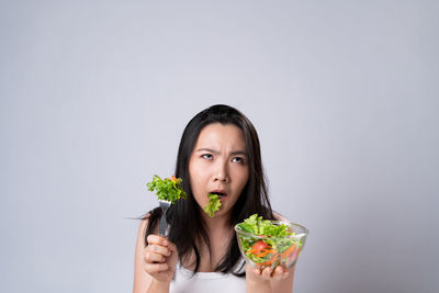 Portrait of young woman eating food against white background