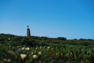 Lighthouse on field against clear blue sky