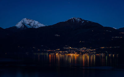 Scenic view of lake by snowcapped mountains against clear sky at night