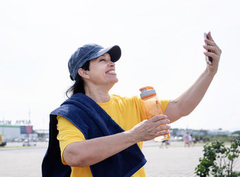 Young woman photographing with mobile phone against sky