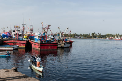 Fishing boats moored at harbor against sky