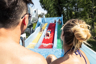 Parents looking at family enjoying water slide in swimming pool