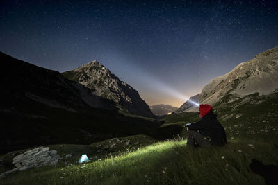 Man sitting on mountain against sky at night