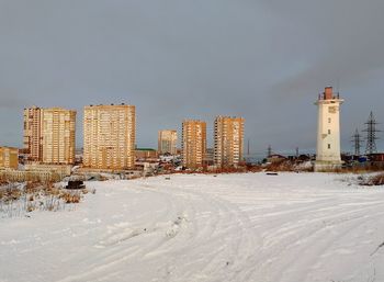 Snow covered field by buildings against sky