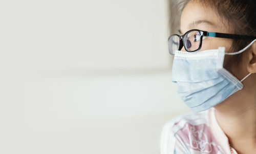 Close-up of girl wearing mask looking away sitting at home