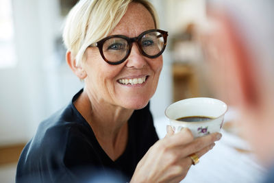 Smiling mature woman holding coffee cup while looking away at home