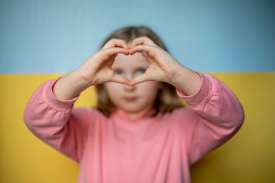 Cute girl making heart shape against wall