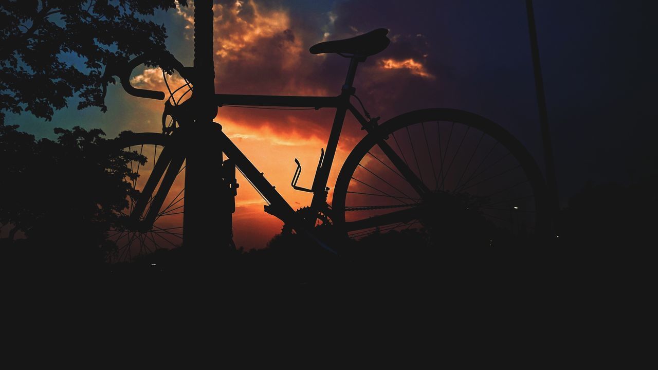 SILHOUETTE OF BICYCLE ON FIELD AGAINST SKY DURING SUNSET