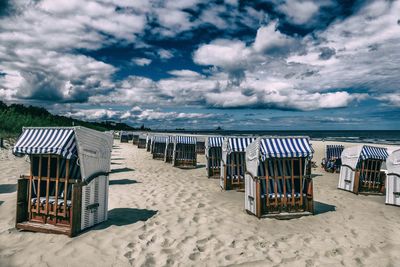 Hooded chairs on beach against sky