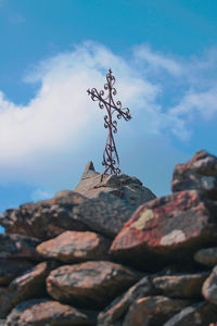 Low angle view of religious cross and rocks against blue sky