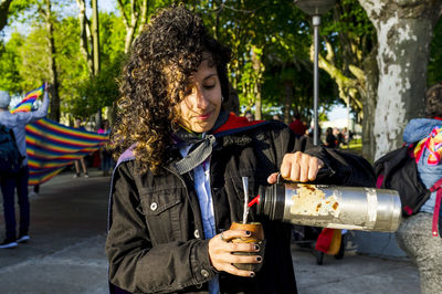 Woman drinking mate and holding a rainbow flag in an lgbtq pride march.