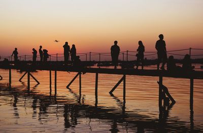 Silhouette people standing on shore against sky during sunset