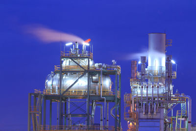 Illuminated factory against blue sky at night