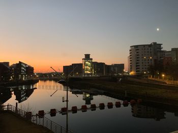 Buildings by river against sky during sunset